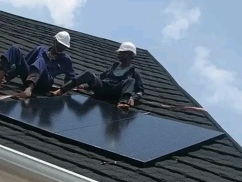 Alzaks technicians in hard hats fitting a solar module to a pitched shingle roof